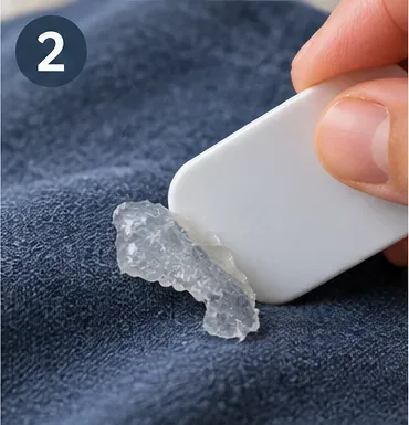 A hand using a smooth plastic card to lift hardened hot glue from blue fabric