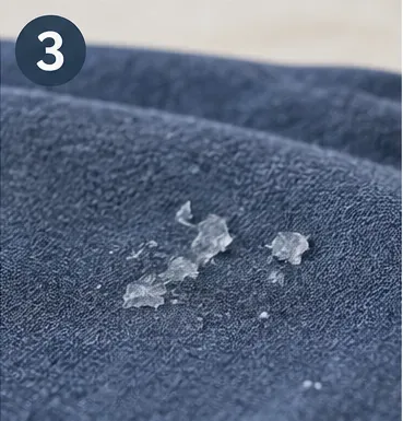 Small translucent pieces of hardened glue remaining on blue fabric after the main blob was removed