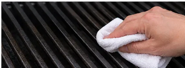 A hand wiping a very thin film of oil across cast iron grill bars
