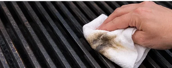 A cloth wiping moisture and residue from black cast iron grill grates
