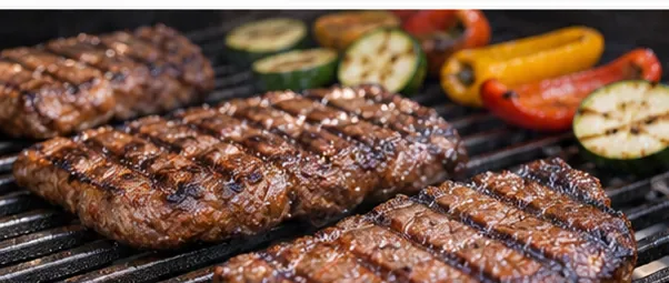 Steaks and vegetables cooking on dark cast iron grill grates