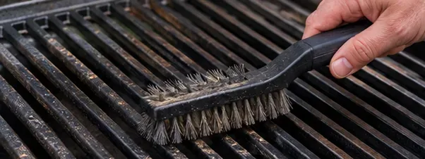 A grill brush removing residue from dark cast iron grill grates