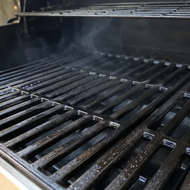 Close-up of lightly oiled cast-iron grill grates giving off wisps of smoke as the oil bakes onto the surface.