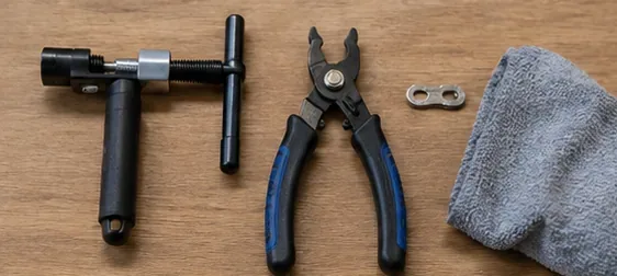 Bicycle chain tool, master-link pliers, spare connector, and shop rag laid out on a workbench