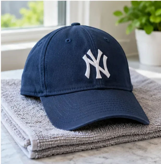 A clean navy baseball cap resting on a folded gray towel near a bright window while air drying