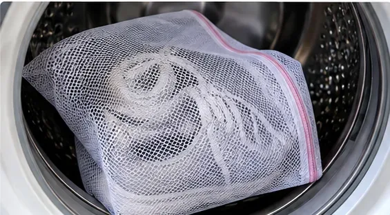 A pair of mesh sneakers enclosed in a zippered laundry bag inside a front-loading washing machine
