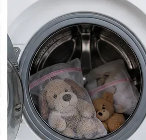Mesh-bagged stuffed animals placed inside a front-loading washing machine with soft towels