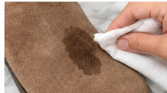 A clean white cloth blotting a fresh dark wet spot on the surface of a brown suede boot