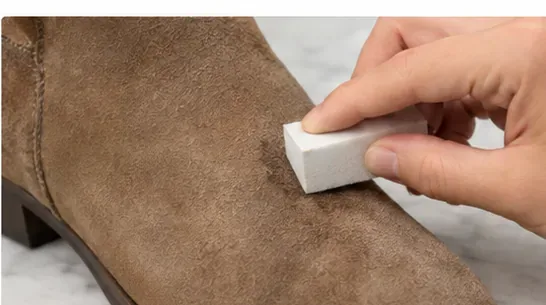 A hand using a clean white suede eraser on a small remaining mark on a tan suede boot