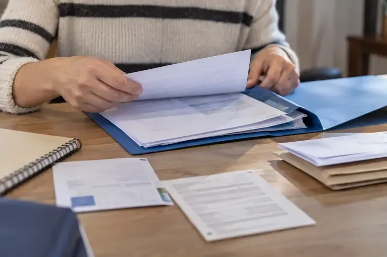 Una persona ordena documentos de identidad y del hogar en una carpeta azul sobre una mesa