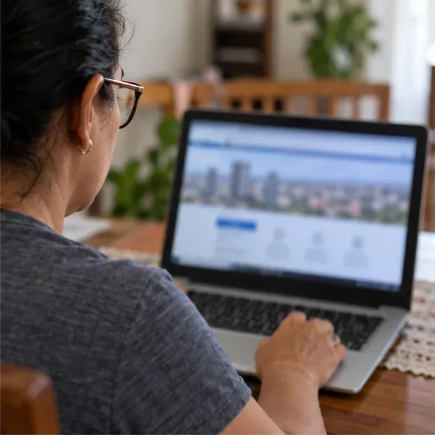 Moradora consulta um site em um notebook; a tela aparece desfocada e sem elementos legíveis.