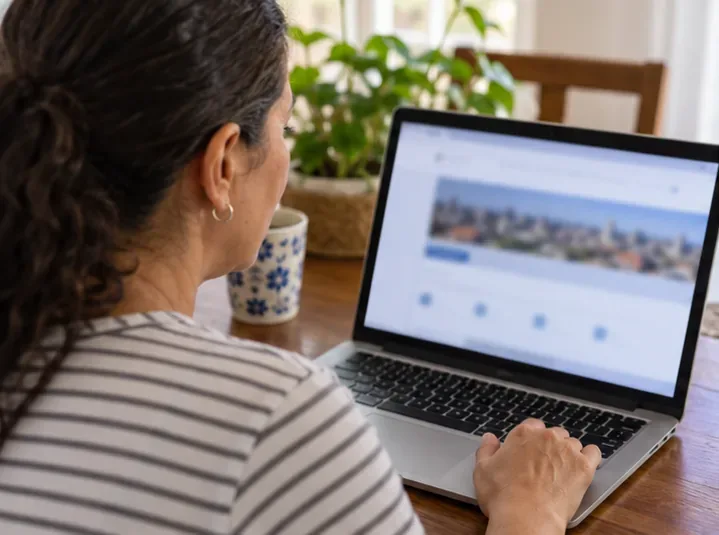 Moradora consulta um serviço municipal em um notebook sobre a mesa de casa