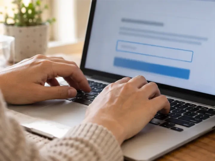 Mãos digitam informações em um formulário aberto no notebook