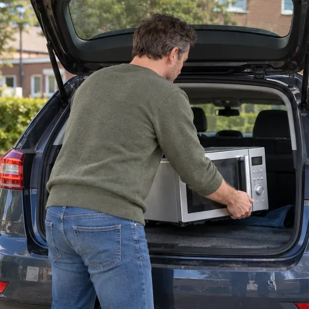 Een bewoner tilt een losgekoppelde magnetron voorzichtig in de kofferbak van een auto