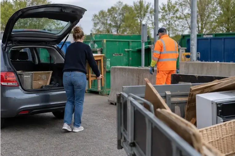 Een inwoner brengt gescheiden huishoudelijk afval uit een auto naar containers op een recyclingterrein