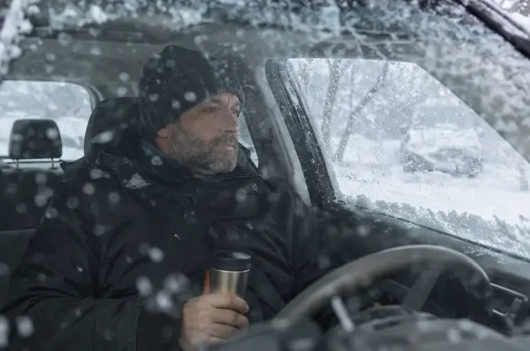 A bundled driver waits inside a parked car during heavy snow