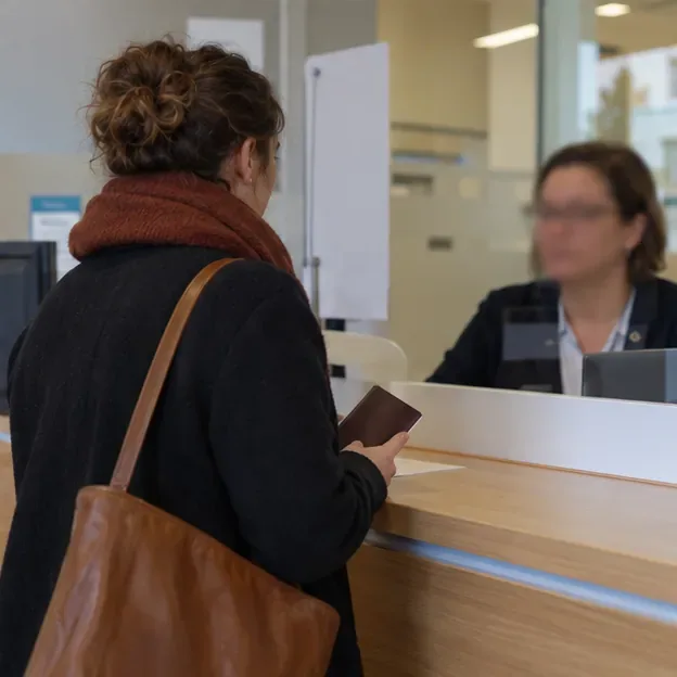Personne présentant une pièce d’identité fermée à un agent derrière un comptoir d’accueil