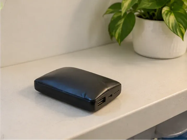 Een opgezwollen zwarte powerbank ligt alleen op een leeg, hard werkblad en is niet aangesloten op een oplader.