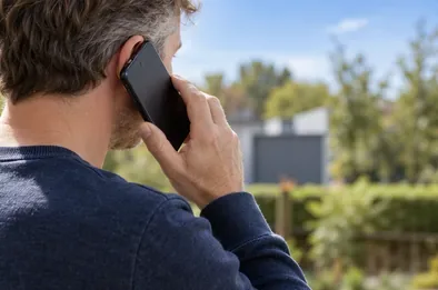 Een volwassene belt met een smartphone vanuit een rustige plek buiten.