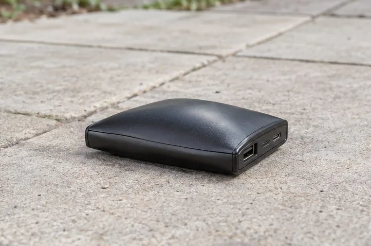 Zwarte powerbank met een zichtbaar bolstaande bovenkant op een kale tegel buiten