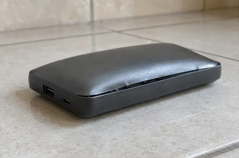 Power bank preto com a carcaça visivelmente abaulada sobre piso cerâmico, indicando bateria interna estufada