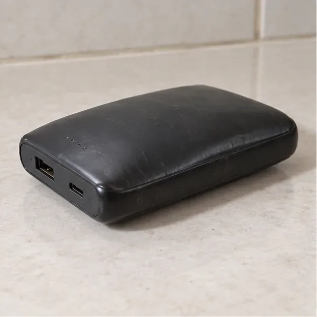 Power bank preto visivelmente estufado sobre uma superfície clara, sem cabo conectado