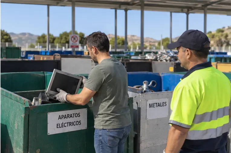 Usuario depositando un aparato electrónico en un contenedor específico mientras un operario supervisa la entrega