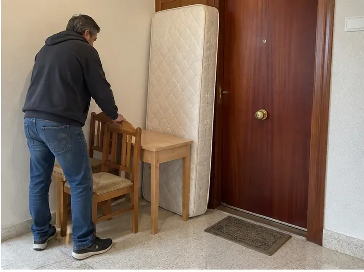 Persona preparando una silla, una mesa pequeña y un colchón dentro del portal antes de la retirada