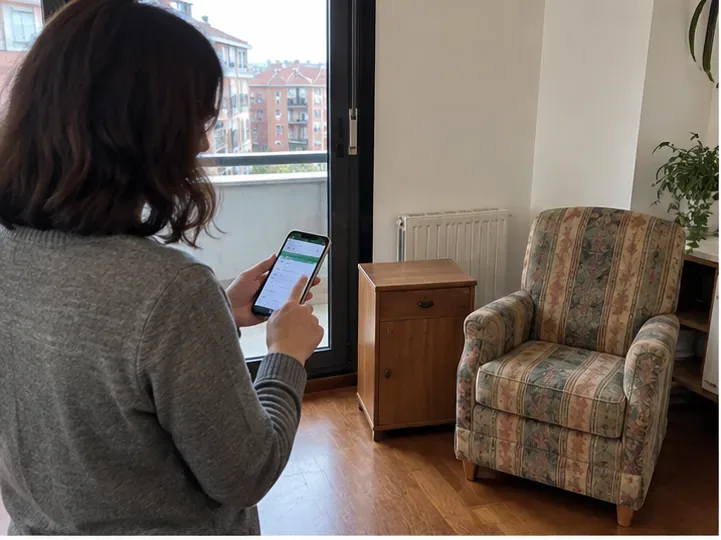 Persona solicitando una cita de recogida desde el móvil junto a un sillón y un mueble que quiere retirar