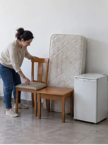Persona revisando y agrupando un colchón, una silla, una mesa y un pequeño electrodoméstico dentro de una vivienda