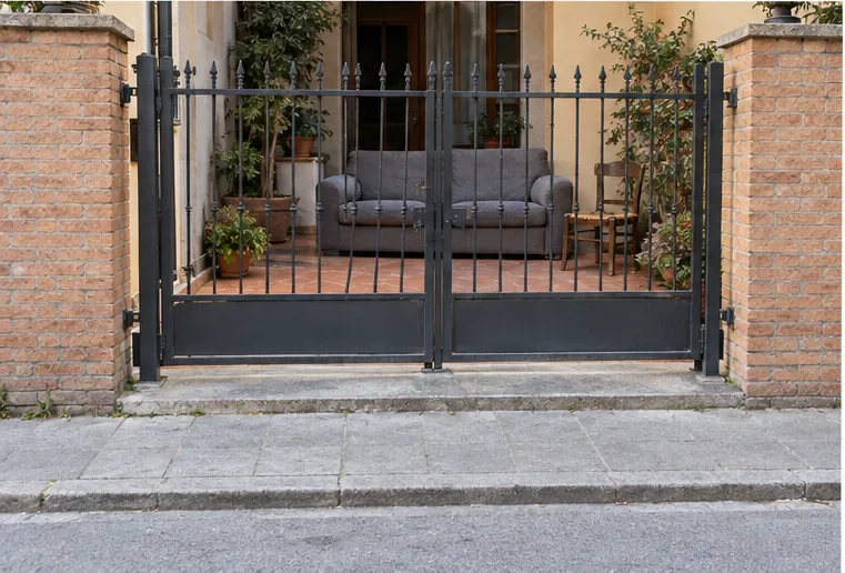Un divano e una sedia sono sistemati all’interno di un cortile privato; il marciapiede esterno al cancello resta libero.