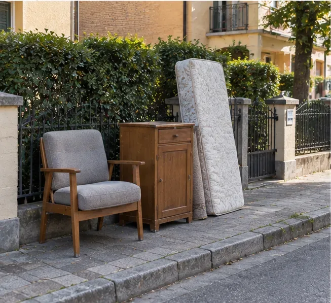 Poltrona, comodino e materasso collocati ordinatamente vicino al bordo della strada per un ritiro prenotato