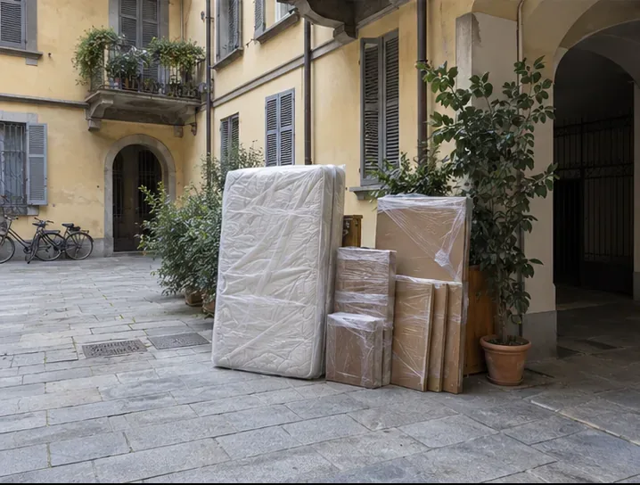 Mobili voluminosi imballati sono disposti ordinatamente in un cortile condominiale.