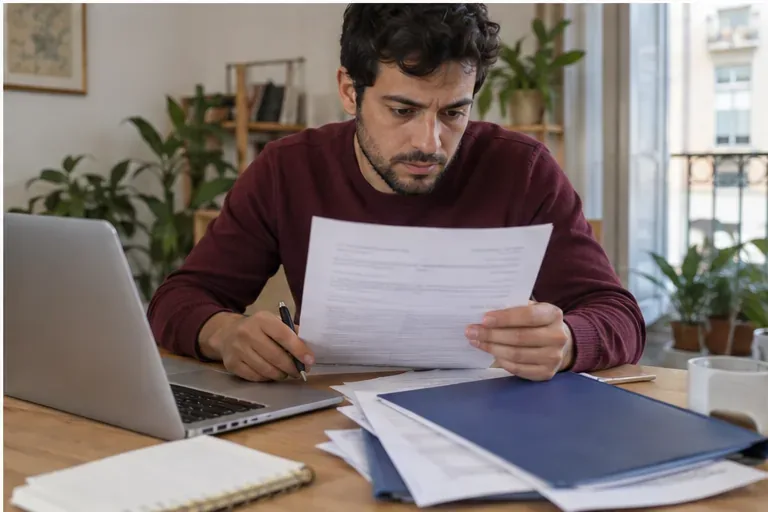 Trabajador preparando documentos junto a un ordenador portátil y una carpeta antes de presentar una reclamación