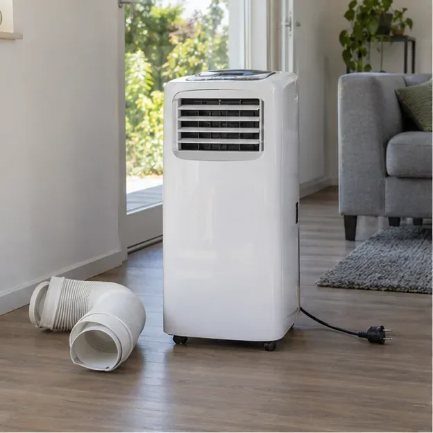 Een draagbare airco staat uitgeschakeld in een woonkamer met de stekker uit het stopcontact en de slang los ernaast.