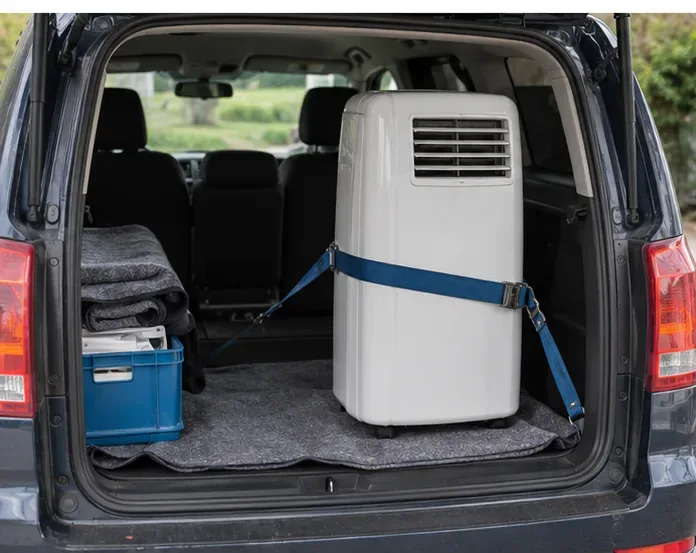Een mobiele airco staat rechtop en met een spanband vastgezet in de laadruimte van een auto.