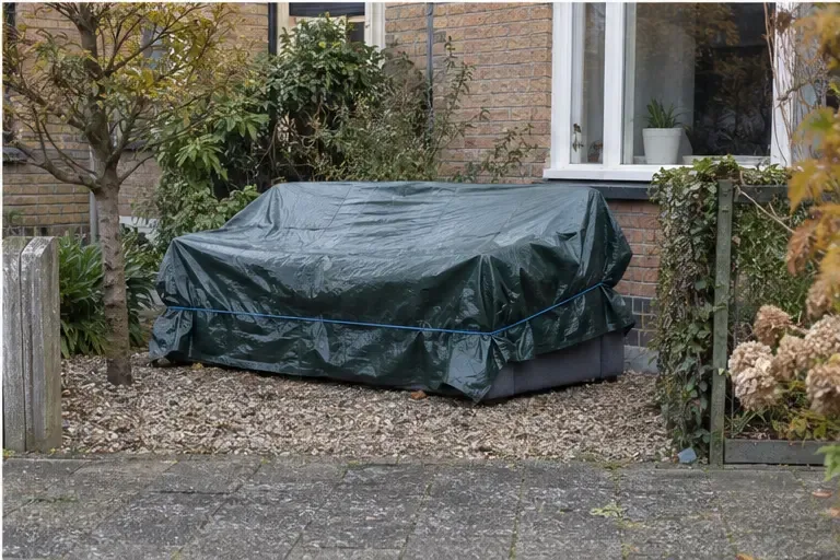 Een bankstel dat onder een afdekzeil in een private voortuin staat, weg van de openbare stoep