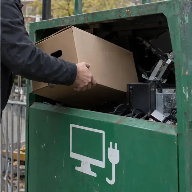 Een oude computer wordt in een inzamelcontainer voor elektrische apparaten geplaatst