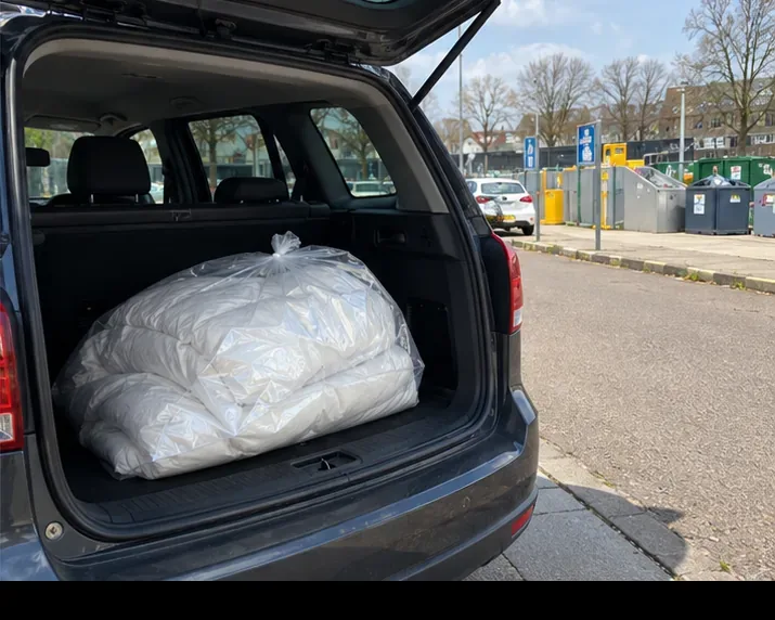 Een zak met dekbed ligt klaar in de auto voor vervoer naar het depot.