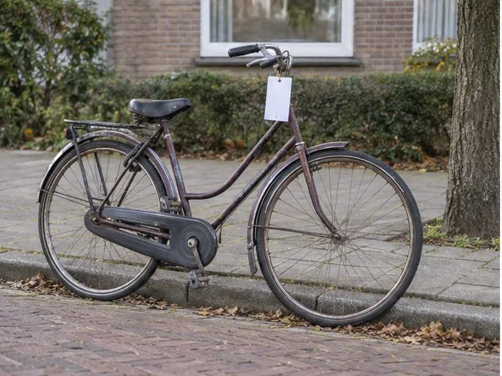 Een oude stadsfiets staat bij de stoep met een blanco kaartje aan het stuur