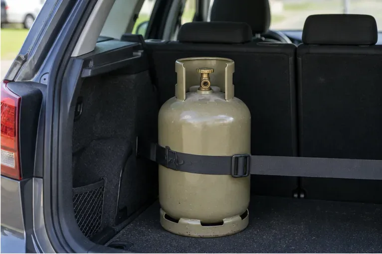 Gasfles die rechtop in de bagageruimte van een auto staat en met een stevige band is vastgezet