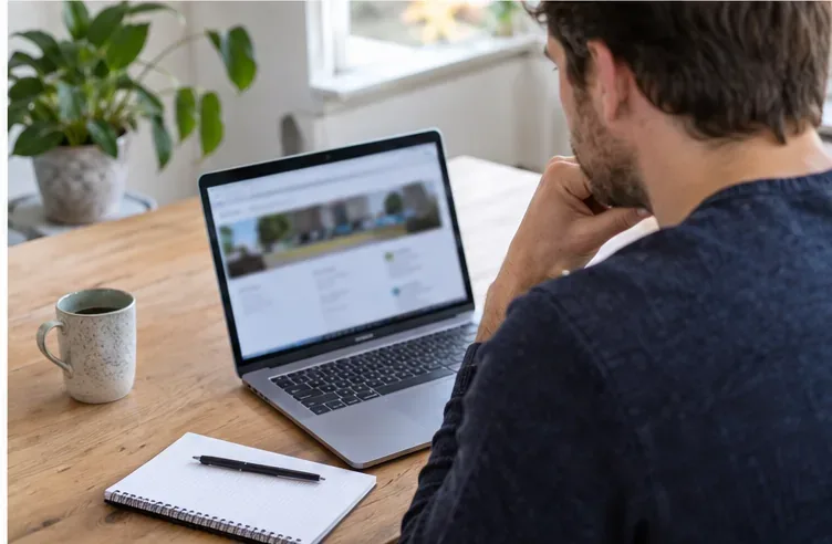 Een persoon bekijkt op een laptop een algemene gemeentelijke afvalpagina en maakt aantekeningen