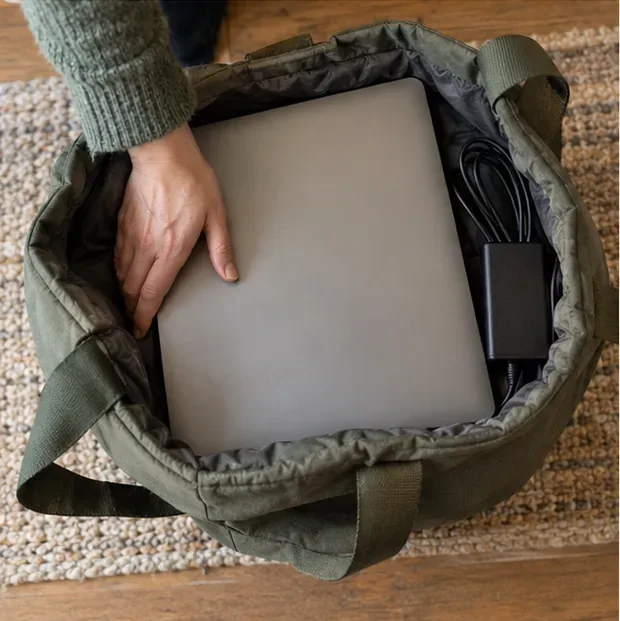 Een gesloten laptop ligt in een gevoerde tas, met de oplader ernaast.
