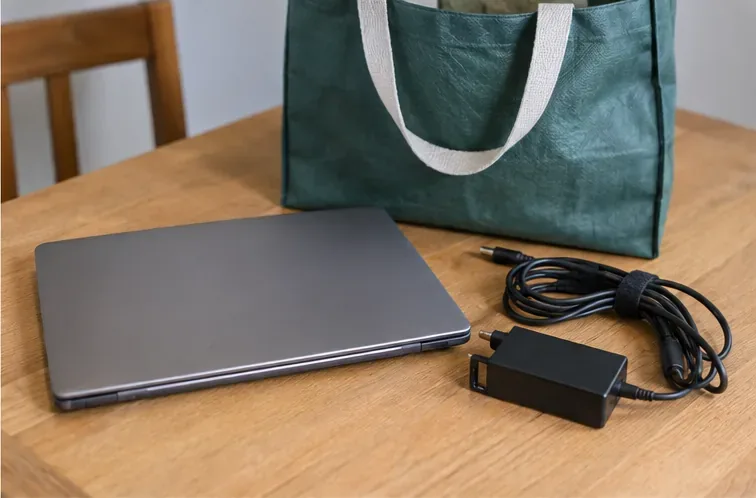 Gesloten laptop met oplader naast een stevige herbruikbare draagtas, klaar om naar een inzamelpunt te brengen
