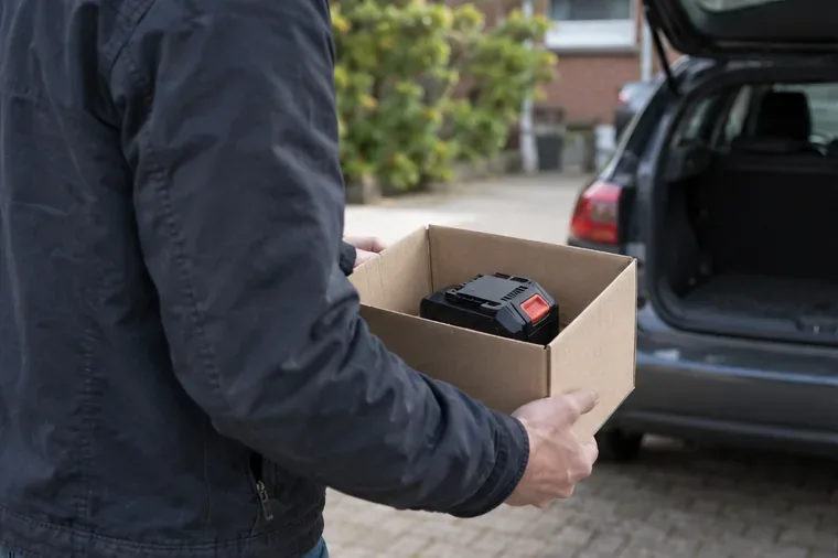 Een inwoner draagt een intacte accu apart in een kartonnen doos naar de auto