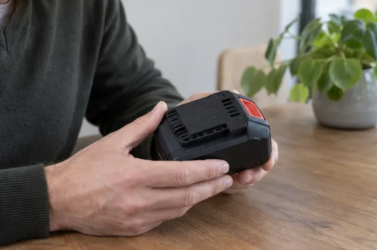 Iemand houdt een losse, onbeschadigde accu van elektrisch gereedschap vast om het type en de staat te controleren