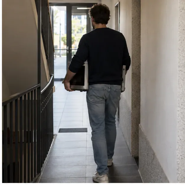 Inwoner draagt een losgekoppelde magnetron door een appartementenhal