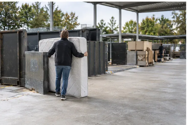 Een bewoner brengt een matras naar een gemeentelijk afvalscheidingsstation