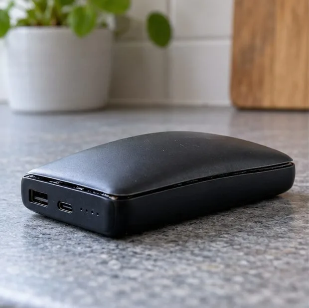 Een zwarte powerbank met een bolstaand deksel en een losgekomen naad ligt onaangeroerd op een stenen aanrecht