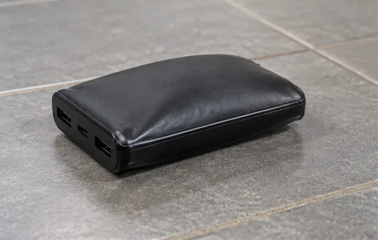 Een zwarte powerbank met duidelijk bolstaande behuizing op een tegelvloer